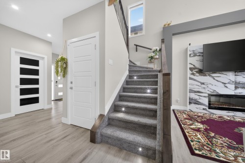 The property features a staircase with carpeted steps and integrated lighting, alongside a living area with a fireplace set into a marble-patterned wall - 449 Roberts Crescent, Leduc, AB - Indoor Photo Showing Other Room