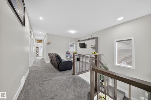The property features a bright hallway with recessed lighting and neutral carpeting, leading to an open area with a window and a staircase featuring wooden handrails and metal balusters - 449 Roberts Crescent, Leduc, AB - Indoor Photo Showing Other Room