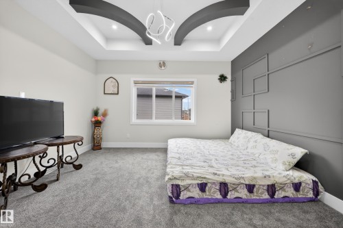This room features a tray ceiling with a contemporary light fixture, plush grey carpeting, and a window providing natural light - 449 Roberts Crescent, Leduc, AB - Indoor Photo Showing Bedroom