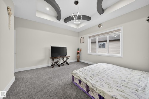 This room features a tray ceiling with accent lighting, a modern light fixture, and plush grey carpeting - 449 Roberts Crescent, Leduc, AB - Indoor Photo Showing Bedroom