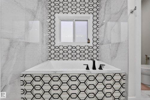 Bathroom featuring a built-in bathtub with black fixtures, geometric patterned tiling, and large format marble-look wall tiles - 449 Roberts Crescent, Leduc, AB - Indoor Photo Showing Bathroom