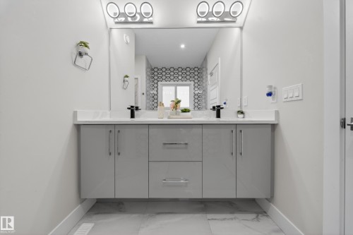 Bathroom featuring a dual vanity with a white countertop, two vessel sinks with matte black faucets, and a large mirror with integrated lighting - 449 Roberts Crescent, Leduc, AB - Indoor Photo Showing Bathroom
