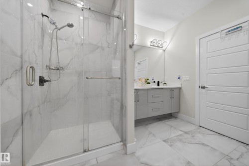 The bathroom features a spacious shower with clear glass enclosure and a vanity with a white countertop and wall-mounted light fixture - 449 Roberts Crescent, Leduc, AB - Indoor Photo Showing Bathroom