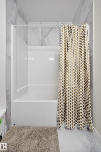Bathroom featuring a white shower and bathtub combination with a subtle marble-patterned tile surround - 449 Roberts Crescent, Leduc, AB - Indoor
