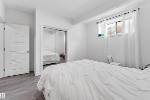 This bedroom features light-toned flooring, a window with white curtains, and a sliding mirrored closet door - 449 Roberts Crescent, Leduc, AB - Indoor Photo Showing Bedroom