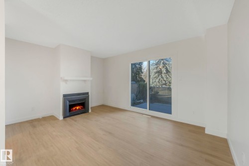 Unfurnished living room featuring light wood finished floors and a warm lit fireplace - 5833 Riverbend Road, Edmonton, AB - Indoor Photo Showing Living Room With Fireplace