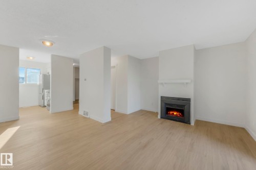 Unfurnished living room with light wood finished floors and a lit fireplace - 5833 Riverbend Road, Edmonton, AB - Indoor Photo Showing Other Room With Fireplace