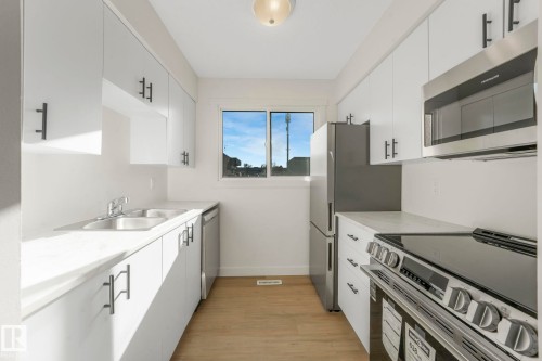 Kitchen with stainless steel appliances, white cabinets, and light wood-style flooring - 5833 Riverbend Road, Edmonton, AB - Indoor Photo Showing Kitchen With Double Sink