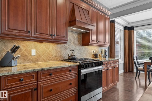 The kitchen features rich wood cabinetry, granite countertops, and a tiled backsplash - 20719 51 Avenue, Edmonton, AB - Indoor Photo Showing Kitchen With Upgraded Kitchen