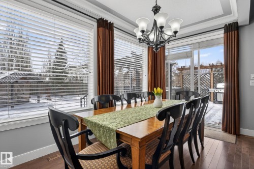 The dining area features a large window offering exterior views, hardwood flooring, and a tray ceiling with a chandelier - 20719 51 Avenue, Edmonton, AB - Indoor Photo Showing Dining Room