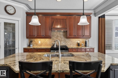 The kitchen features rich wood cabinetry, a patterned tile backsplash, and a spacious island with a granite countertop and an integrated sink - 20719 51 Avenue, Edmonton, AB - Indoor Photo Showing Kitchen With Double Sink With Upgraded Kitchen