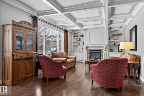 Living area featuring hardwood flooring, a coffered ceiling, a fireplace with a stone surround, and built-in shelving - 20719 51 Avenue, Edmonton, AB - Indoor With Fireplace