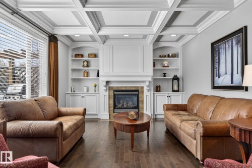 Living room featuring coffered ceilings, dark hardwood floors, and a fireplace with a stone surround and ornate white mantle - 20719 51 Avenue, Edmonton, AB - Indoor Photo Showing Living Room With Fireplace