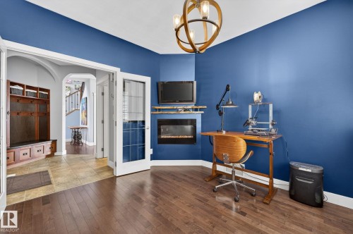 This interior space features hardwood flooring and a fireplace, with double doors leading to an entryway with tiled flooring - 20719 51 Avenue, Edmonton, AB - Indoor With Fireplace
