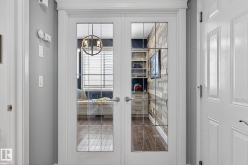 French doors with glass paneling open to a room featuring a built-in window seat, a wall-mounted television, and wood-paneled walls - 20719 51 Avenue, Edmonton, AB - Indoor Photo Showing Other Room