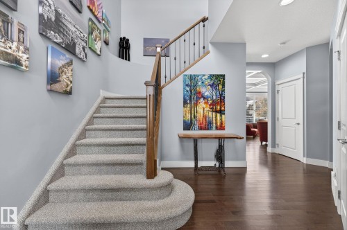 The property features a staircase with carpeted steps and a wooden handrail with black balusters, alongside rich hardwood flooring in the hallway - 20719 51 Avenue, Edmonton, AB - Indoor Photo Showing Other Room