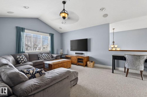 Inviting living space featuring a vaulted ceiling with a decorative light fixture, carpeted flooring, and a large window with blinds - 20719 51 Avenue, Edmonton, AB - Indoor Photo Showing Living Room