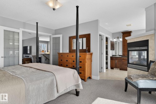 This bedroom features light gray walls, a carpeted floor, and a fireplace with a light-colored tile surround - 20719 51 Avenue, Edmonton, AB - Indoor Photo Showing Bedroom