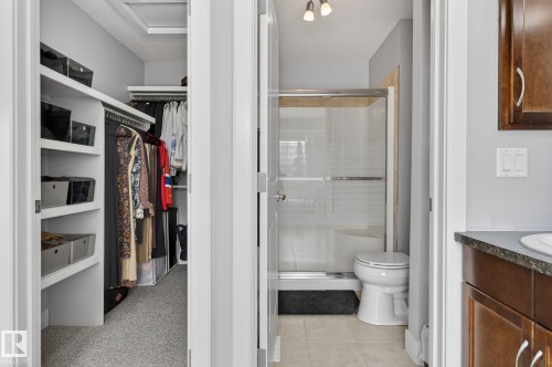 The property includes a walk-in closet with built-in shelving, a bathroom with a glass-enclosed shower, a toilet, and a vanity with a dark countertop and wooden cabinetry - 20719 51 Avenue, Edmonton, AB - Indoor Photo Showing Bathroom
