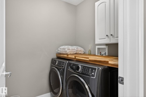 This laundry area features white upper cabinetry, a light wood countertop, and gray walls - 20719 51 Avenue, Edmonton, AB - Indoor Photo Showing Laundry Room