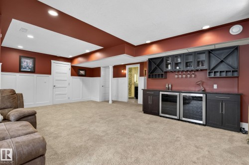 Spacious room featuring plush carpeting, a built-in wet bar with dark cabinetry, two under-counter beverage refrigerators, and recessed lighting - 20719 51 Avenue, Edmonton, AB - Indoor