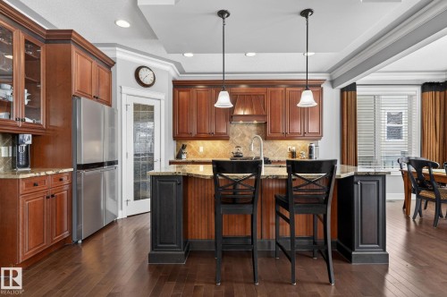 The kitchen features wood cabinetry, stainless steel appliances, and a central island with a granite countertop - 20719 51 Avenue, Edmonton, AB - Indoor Photo Showing Kitchen With Stainless Steel Kitchen With Upgraded Kitchen