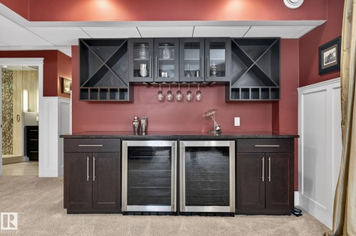 This area features a built-in bar with dark cabinetry, a stone countertop, and two under-counter beverage refrigerators - 20719 51 Avenue, Edmonton, AB - Indoor Photo Showing Other Room