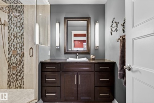 The bathroom features a spacious vanity with a dark wood finish and a white vessel sink, complemented by a large mirror and vertical lighting fixtures - 20719 51 Avenue, Edmonton, AB - Indoor Photo Showing Bathroom