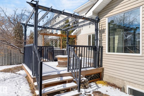 The property features a wooden deck with black railings and steps, partially covered by a dark pergola with string lights - 20719 51 Avenue, Edmonton, AB - Outdoor With Deck Patio Veranda With Exterior