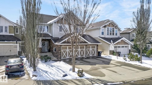 The property features a stone and siding exterior with a multi-car garage, a paved driveway, and mature trees - 20719 51 Avenue, Edmonton, AB - Outdoor With Facade