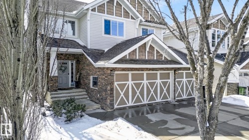 The property presents an appealing exterior with stone cladding and siding, featuring a covered front entrance and a double garage with decorative doors - 20719 51 Avenue, Edmonton, AB - Outdoor With Facade