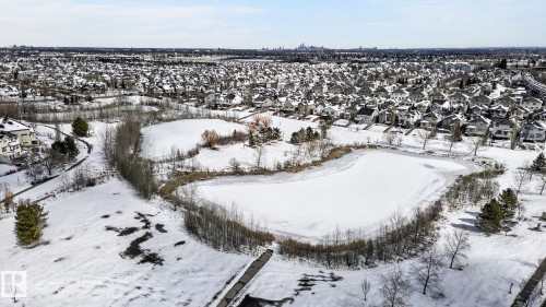 This aerial view showcases the property's proximity to a residential area with snow-covered rooftops, two frozen ponds, and a walking path - 20719 51 Avenue, Edmonton, AB - Outdoor With View