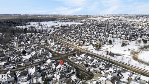 Aerial view of the surrounding neighborhood, featuring residential properties with dark roofs, local roads, and nearby natural areas including wooded sections and a frozen pond - 20719 51 Avenue, Edmonton, AB - Outdoor With View