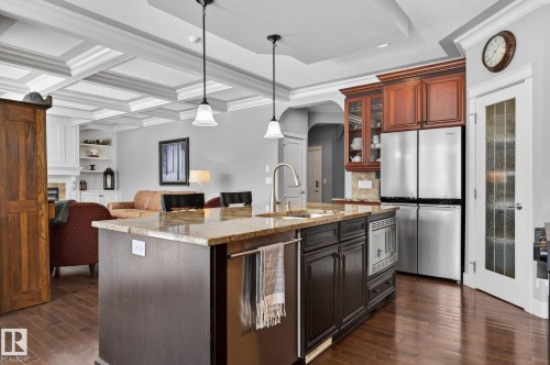 The kitchen features a center island with a granite countertop, a stainless steel sink with a gooseneck faucet, and dark wood cabinetry with a built-in microwave - 20719 51 Avenue, Edmonton, AB - Indoor Photo Showing Kitchen With Stainless Steel Kitchen With Upgraded Kitchen