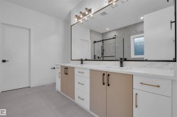 Bathroom featuring a spacious double vanity with two sinks, dark matte faucets, and a large mirror with contemporary lighting fixtures - 