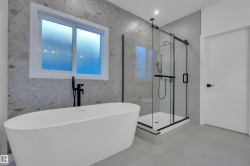 Bathroom featuring a freestanding white bathtub, a walk-in shower with a glass enclosure, a white framed window, and light-toned walls with a speckled pattern - 