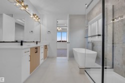 The bathroom features a double vanity with two sinks, modern light fixtures, a freestanding soaking tub, and a glass-enclosed shower - 