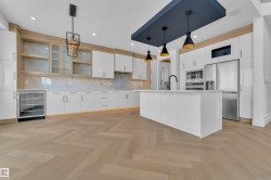 The kitchen features a large island, white cabinetry, a built-in refrigerator, and a beverage cooler - 