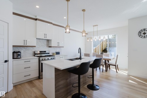 The kitchen features white cabinetry, a large island with seating, a stainless steel range, and light wood flooring - 79 Silverstone Drive, Stony Plain, AB - Indoor Photo Showing Kitchen With Double Sink With Upgraded Kitchen