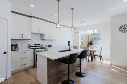 The kitchen features white cabinetry, a large island with seating, a stainless steel range, and light wood flooring - 