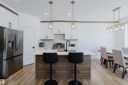 The kitchen features a center island with seating, a stainless steel refrigerator, white cabinetry, and a gas range - 
