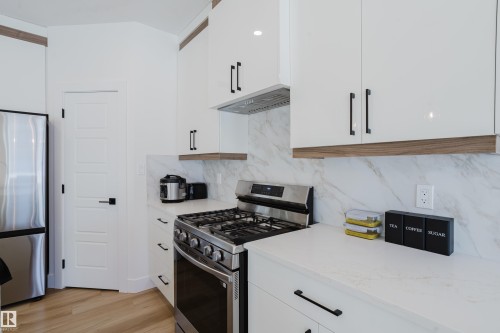 Modern kitchen with white cabinetry, stainless steel appliances, marble-look backsplash, and light wood flooring - 79 Silverstone Drive, Stony Plain, AB - Indoor Photo Showing Kitchen