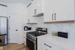 Modern kitchen with white cabinetry, stainless steel appliances, marble-look backsplash, and light wood flooring - 