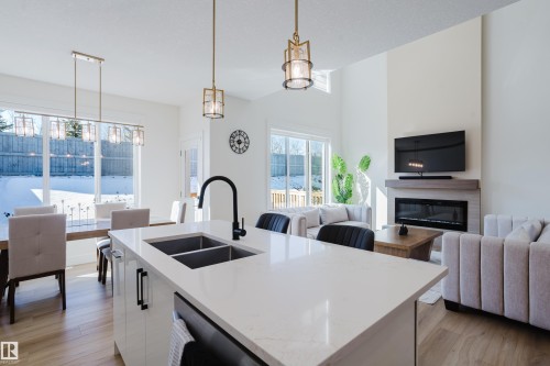 The property features an open-concept living area with a kitchen island, a fireplace, and large windows providing abundant natural light - 79 Silverstone Drive, Stony Plain, AB - Indoor Photo Showing Kitchen With Fireplace With Double Sink With Upgraded Kitchen