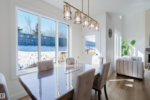 The dining area features a rectangular dining table with seating, a linear chandelier with glass shades, and large windows offering views of the outdoors - 79 Silverstone Drive, Stony Plain, AB - Indoor Photo Showing Dining Room