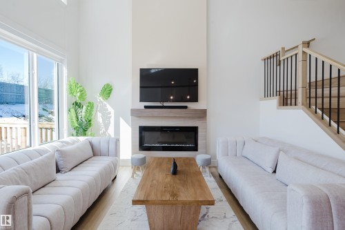 Bright living area featuring a fireplace, large windows providing natural light, and light-colored flooring - 79 Silverstone Drive, Stony Plain, AB - Indoor Photo Showing Living Room With Fireplace