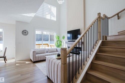 The property offers an open concept living area with high ceilings, large windows providing natural light, light wood-toned flooring, and a fireplace - 79 Silverstone Drive, Stony Plain, AB - Indoor Photo Showing Other Room