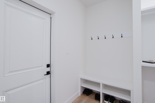 Entryway featuring a white paneled door with matte black hardware, built-in storage bench with open shelving, and wall-mounted coat hooks - 79 Silverstone Drive, Stony Plain, AB - Indoor Photo Showing Other Room