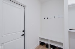 Entryway featuring a white paneled door with matte black hardware, built-in storage bench with open shelving, and wall-mounted coat hooks - 