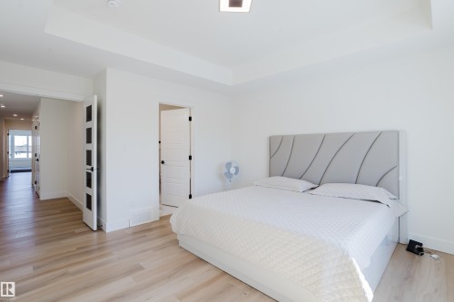 This sleeping area features light-toned hardwood flooring, white walls, and a modern upholstered headboard - 79 Silverstone Drive, Stony Plain, AB - Indoor Photo Showing Bedroom